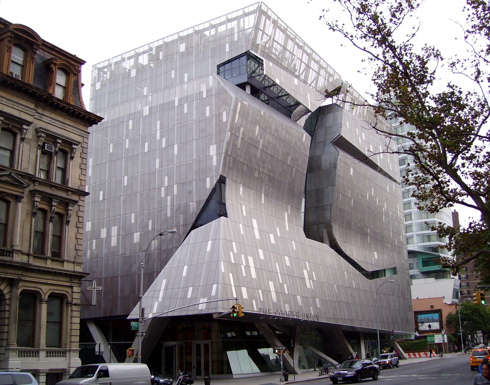41 Cooper Square 自北側望向街角，穿孔不鏽鋼外皮上有開啟中的活動板，右側一道大缺口被撕開