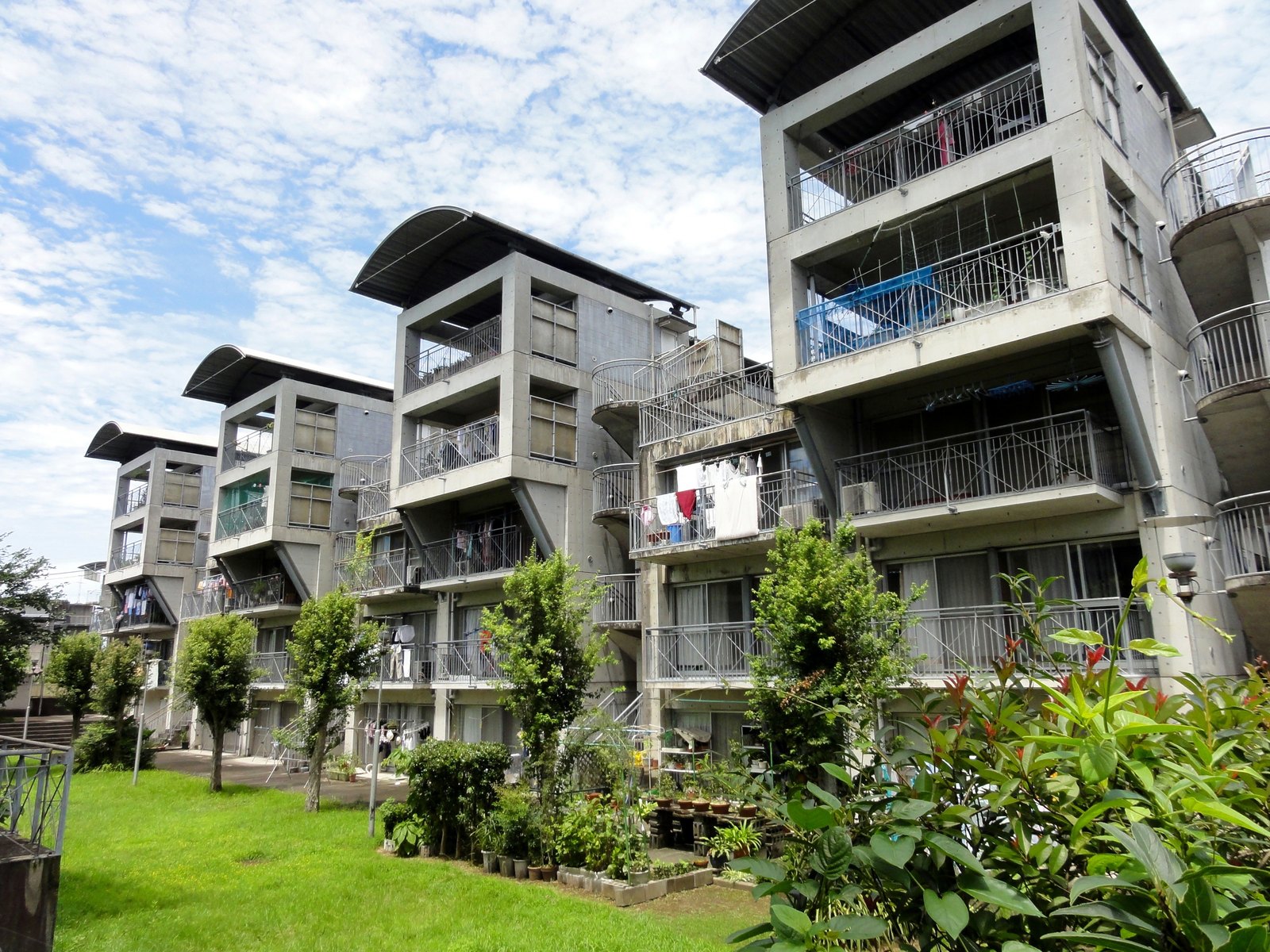 熊本縣營保田窪第一團地，從中庭側望向住棟，陽台上曬著衣物、地面有住戶種的盆栽