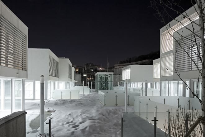 Pangyo Housing 二樓共用甲板的夜景,兩側是亮著燈的玻璃玄關,甲板上有積雪