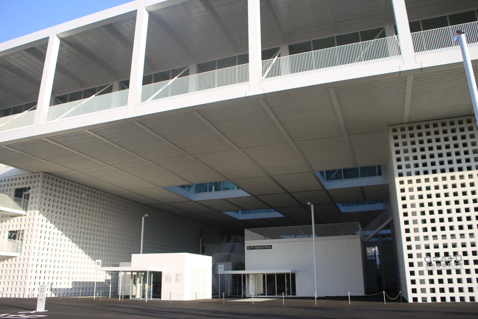 名古屋造形大學名城公園校區，架空的校舍量體下方是完全開放的地面層，白色量體上有規則的方形開孔