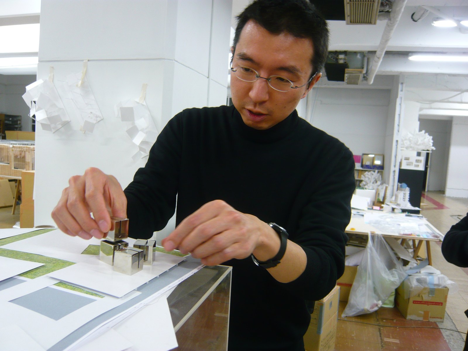建築師藤本壯介在事務所裡用雙手排列一組金屬方塊模型